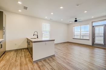 An empty living room with a kitchen and a window